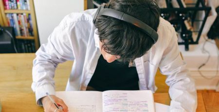 jeune homme porte un casque audio et travaille sur cahier et ordinateur