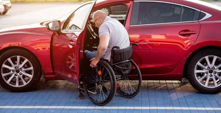 Une personnes handicapée accède à sa voiture sur une place de parking PMR.