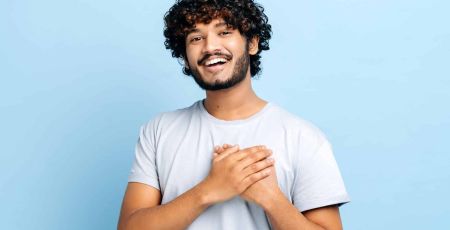 Un homme en t-shirt bleu sourit et a les deux mains sur le coeur