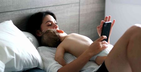 Une maman utilisant l'application May alors que son bébé dort contre elle.