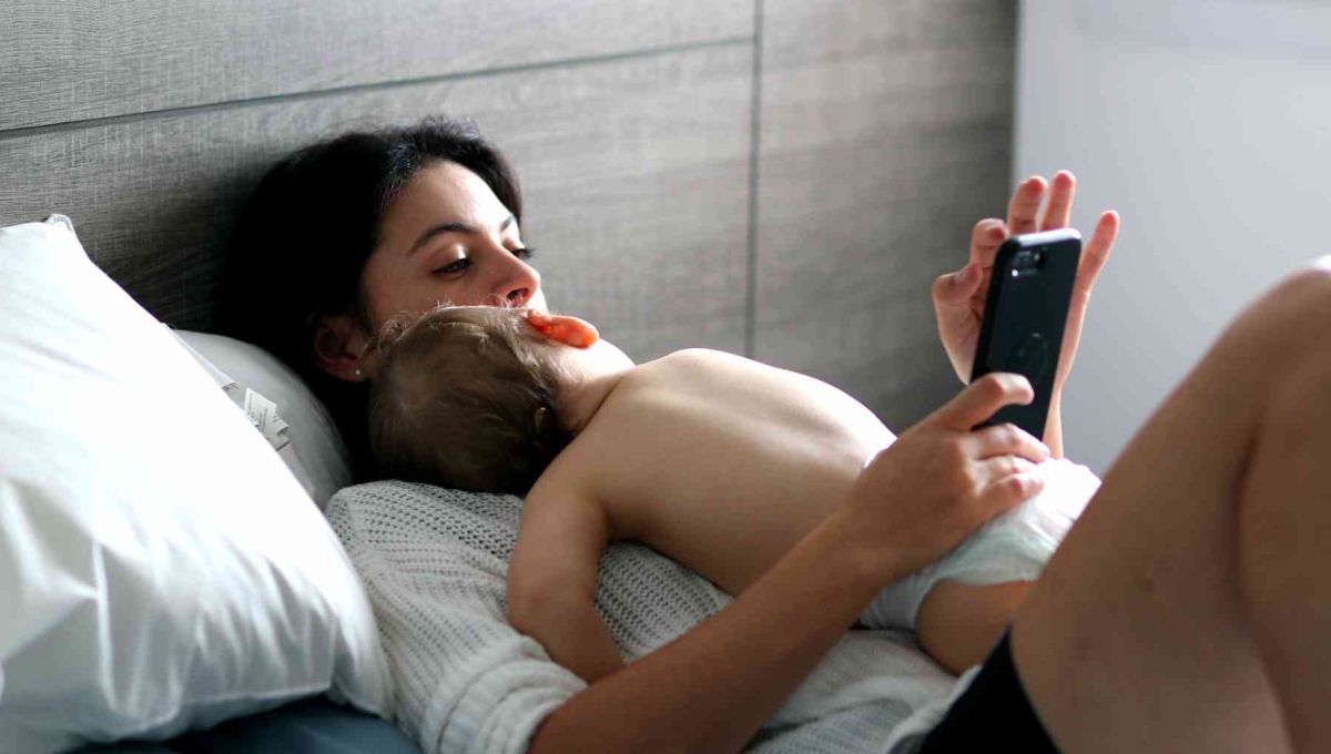 Une maman utilisant l'application May alors que son bébé dort contre elle.