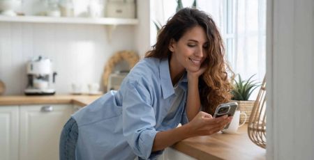 Une femme sourit en regardant son téléphone.