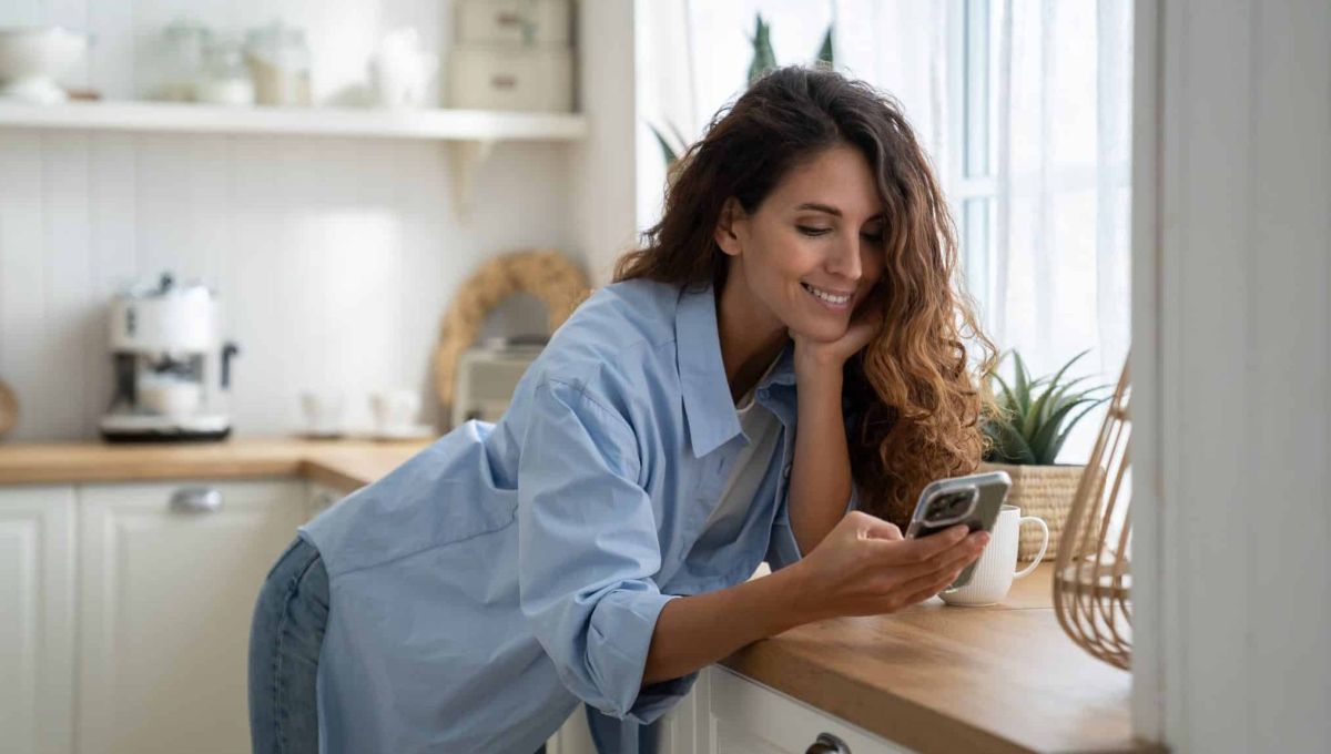Une femme sourit en regardant son téléphone.