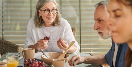 Une femme attablée mange du raisin.