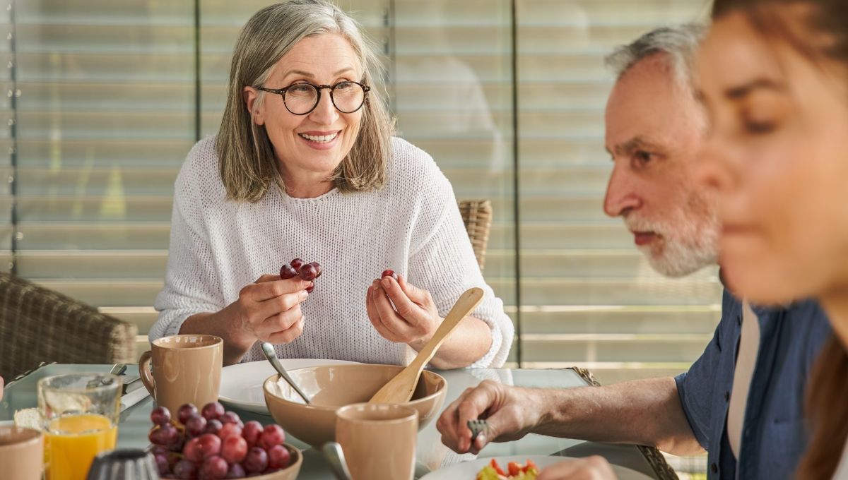 Une femme attablée mange du raisin.