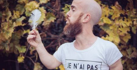 Un homme barbu de petite taille souffle sur une plume blanche