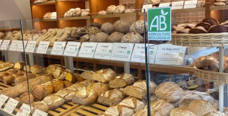 Dans une boulangerie, un étal rempli de pains avec la mention "Agriculture Biologique"