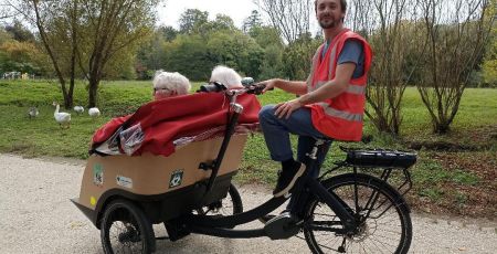 Un bénévole de l'association A vélo sans âge pilote un triporteur dans un parc.