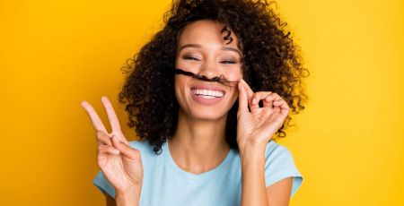 femme qui sourit avec les doigts en signe de victoire et qui fait semblant d'avoir une moustache avec ses cheveux