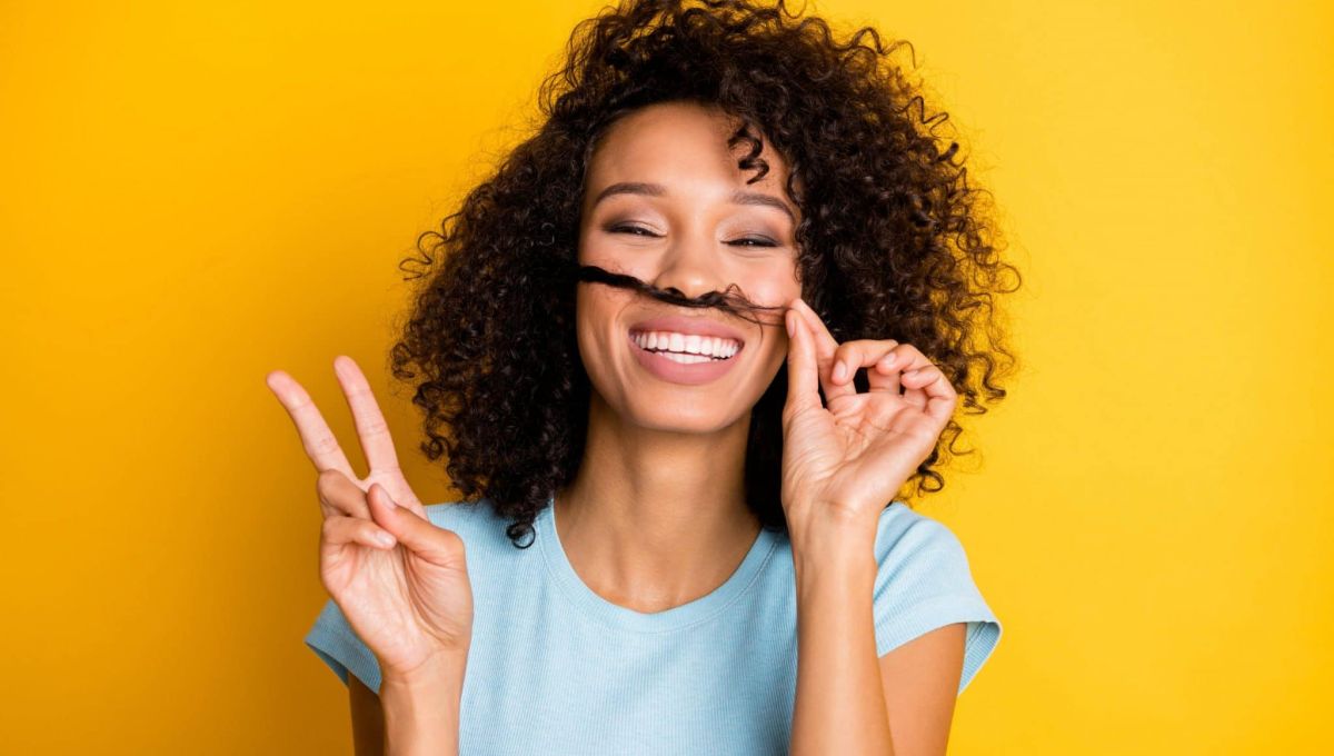 femme qui sourit avec les doigts en signe de victoire et qui fait semblant d'avoir une moustache avec ses cheveux