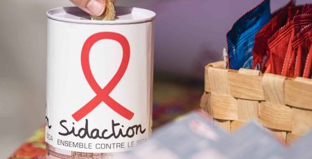 Une personne fait un don d'une pièce dans une tirelire Sidaction
