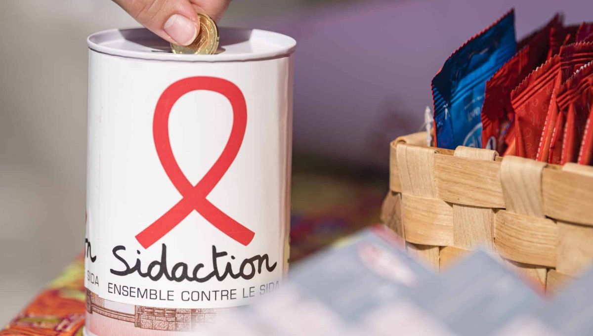 Une personne fait un don d'une pièce dans une tirelire Sidaction