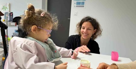 Une petite fille mange un yaourt, encouragée par ses thérapeutes