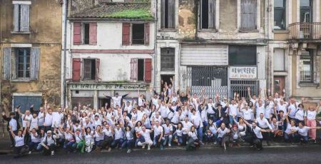 L'équipe d'investir ensemble pose dans la rue devant plusieurs habitations. Les gens portent un t-shirt blanc et ont l'air content.