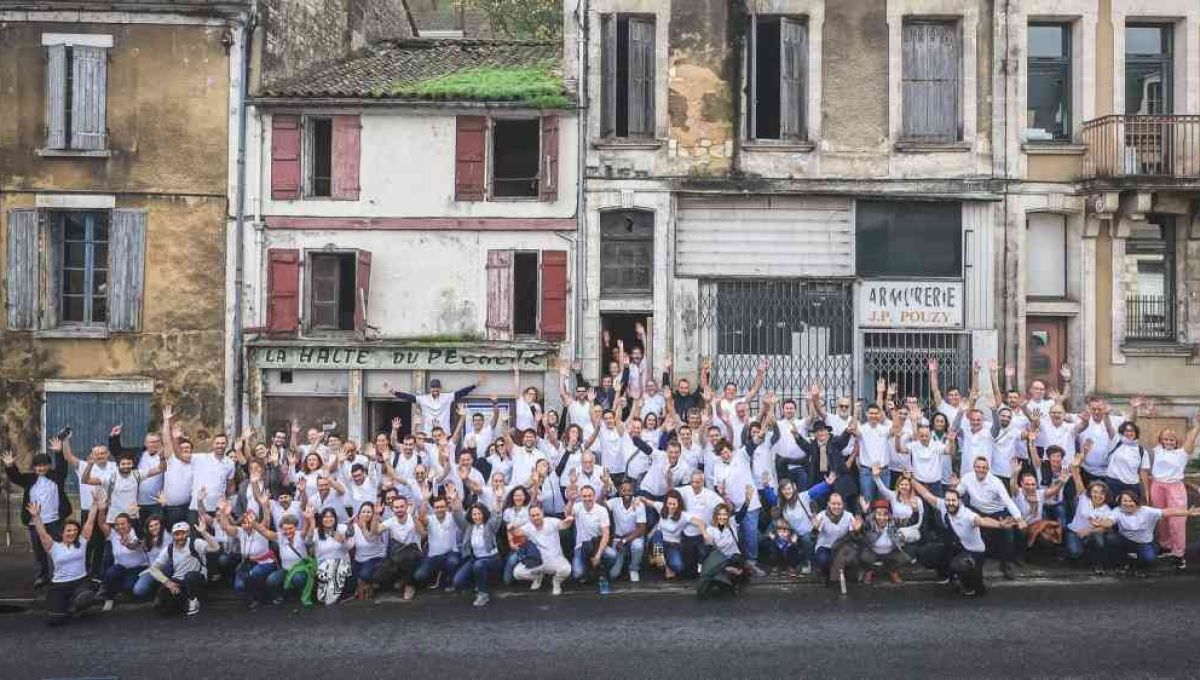 L'équipe d'investir ensemble pose dans la rue devant plusieurs habitations. Les gens portent un t-shirt blanc et ont l'air content.