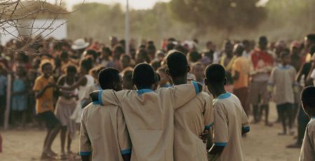 Quatre enfants à madagascar, heureux, de dos devant une foule