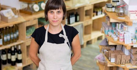 Cherfull young female shop owner posing in front of shelves full of healthy products.
