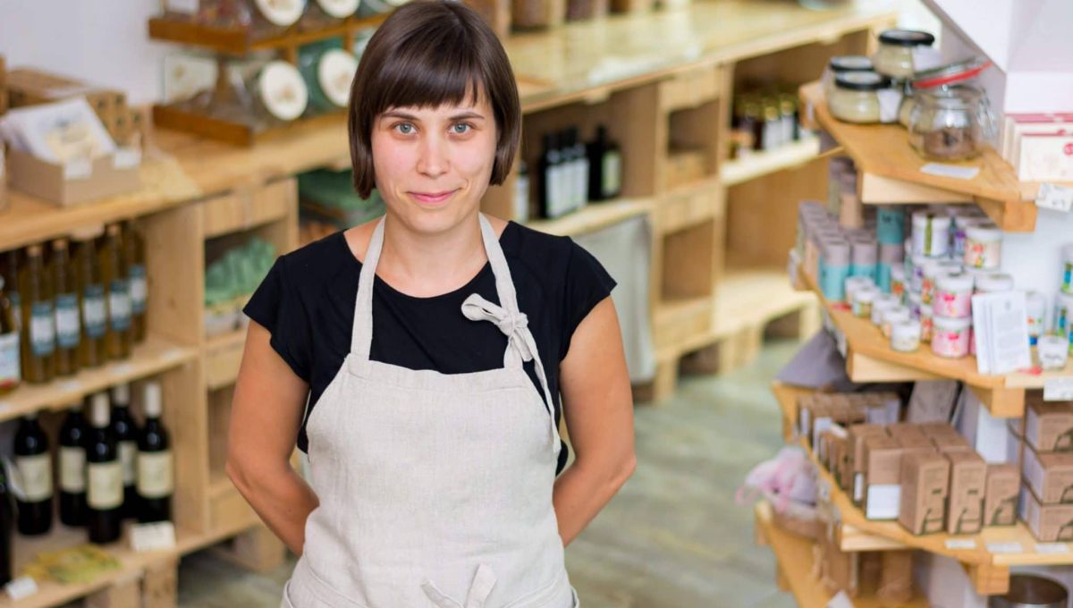 Cherfull young female shop owner posing in front of shelves full of healthy products.