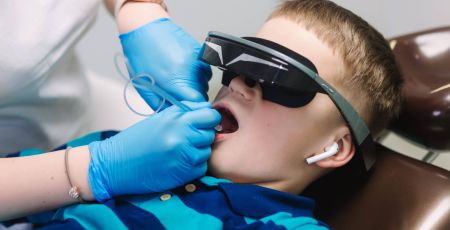 Close up of little boy sitting in dentist in vr glasses and wireless headphones while dentist make x-ray of teeth