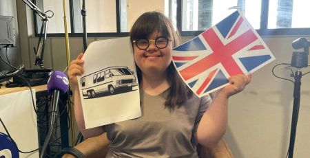 Jeanne avec un drapeau anglais dans la main droite et une image de camping-car dans la main gauche.