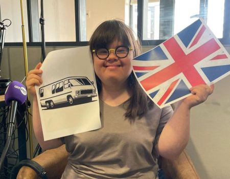 Jeanne avec un drapeau anglais dans la main droite et une image de camping-car dans la main gauche.