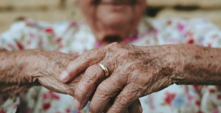 au premier plan il y a les mains jointes d'une personne âgée