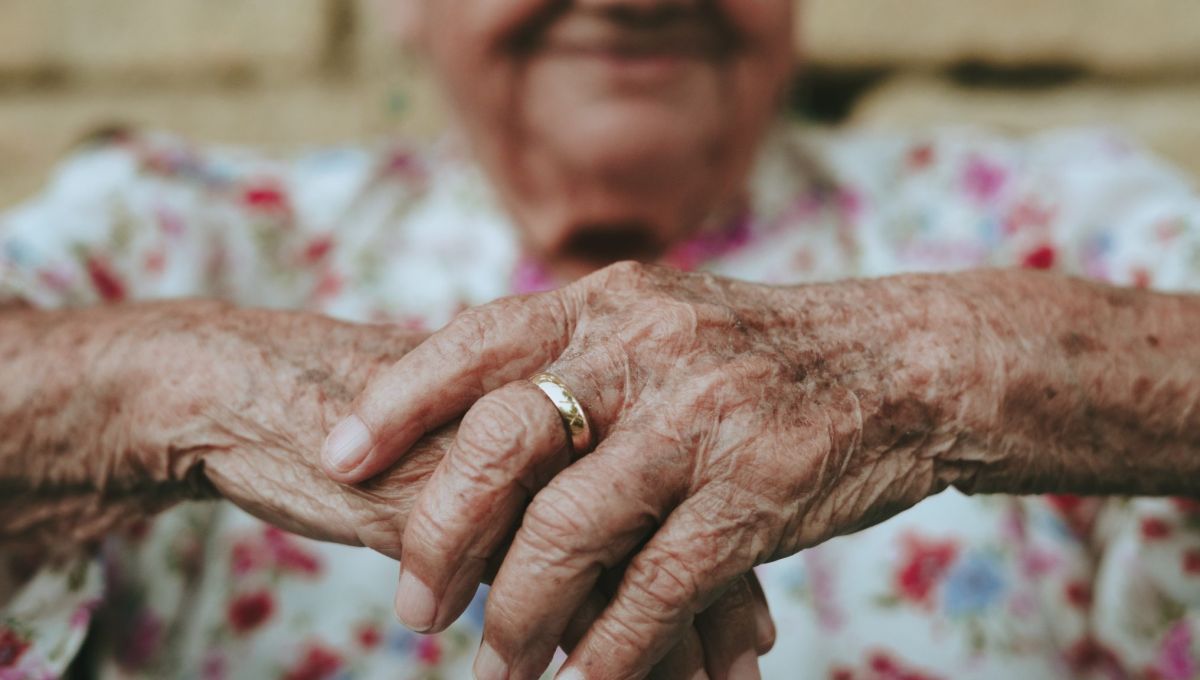 au premier plan il y a les mains jointes d'une personne âgée