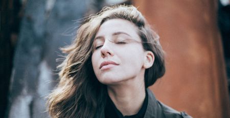 Une femme ferme les yeux, elle a le vent dans ses cheveux