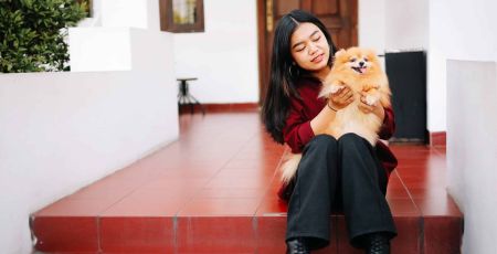 Une femme est assise sur des escaliers elle joue avec un chien