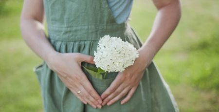 gardening and profession concept - young woman in apron holding flowers in the garden in summer