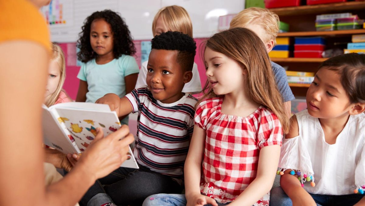 Group Of Elementary School Pupils Sitting On Floor Listening To Female Teacher Read Story