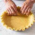 Mains en train de foncer un moule avec une pâte à tarte