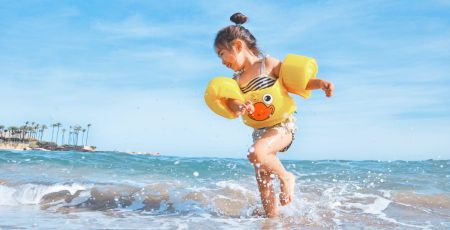 Une petite fille brune cours dans l'eau en maillot de bain avec des bouées autour d'elle