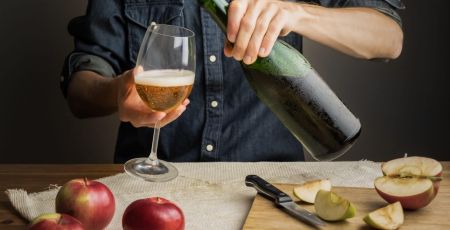 Male hands pouring premium cidre in wine glass above rustic wood table. Tasting vintage apple cider out of ice cold bottle