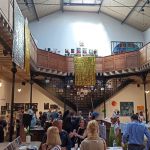 Photo de l'intérieur du Bastille design center. Il s'agit d'une grande pièce avec une importante hauteur sous plafond. L'étage est constitué d'une coursive en bois, sur piliers métalliques, qui fait le tour de la salle.
