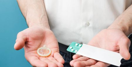 Male contraceptives. Pills and condom in hands of men