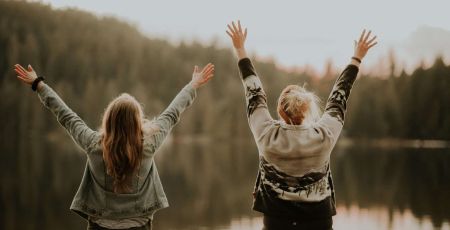 Deux femmes les bras en l'air font face à un lac et expriment leur bonheur