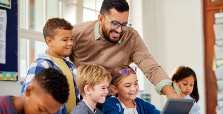 Des enfants et un professeur à l'école avec une tablette en classe.
