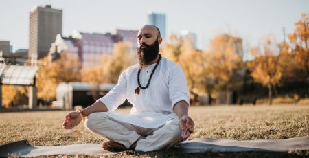 Un homme est assis par terre sur un tapis de yoga. Il a les yeux fermés.