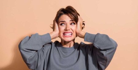 Santé auditive : quelles solutions pour limiter les nuisances sonores ? Une femme grimace. Elle met ses mains sur ses oreilles.