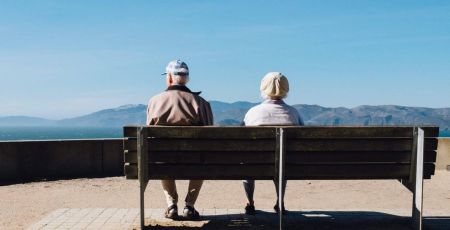 deux personnes âgées assisent sur un banc face à une montagne