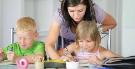 Mère qui aide ses deux enfants souriants à faire les devoirs.