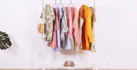 Women's hip clothing store interior concept. Row of different colorful female clothes hanging on rack in hipster fashion show room in shopping mall. White wall background. Copy space.